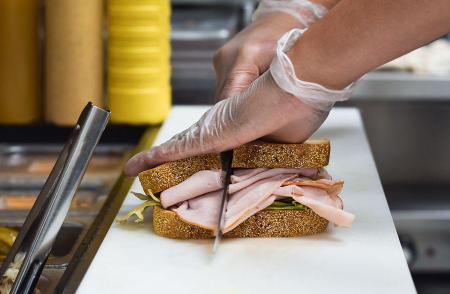 Restaurant kitchen employee in gloves cutting a sandwich